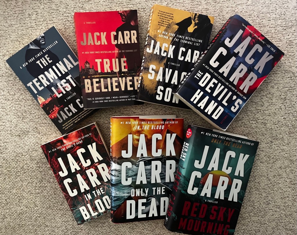 Jack Carr’s Terminal List series arranged together on a neutral textured background, featuring seven thriller novels including The Terminal List, True Believer, Savage Son, The Devil’s Hand, In the Blood, Only the Dead, and Red Sky Mourning.